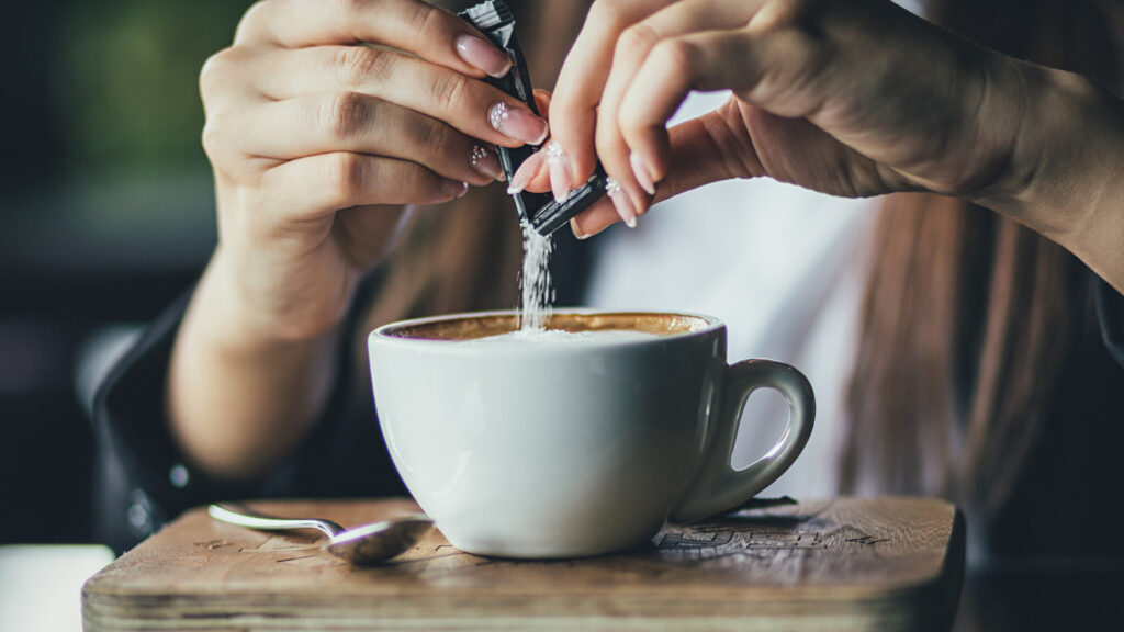 The Girl's Hand Pours Sugar Into Her Coffee. Close Up